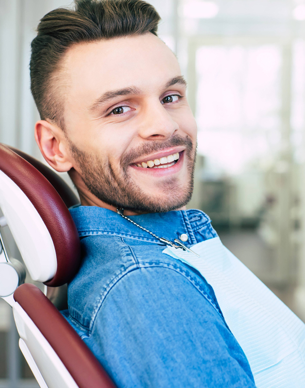 Smiling man in denim shirt sitting in dental chair at modern dental office
